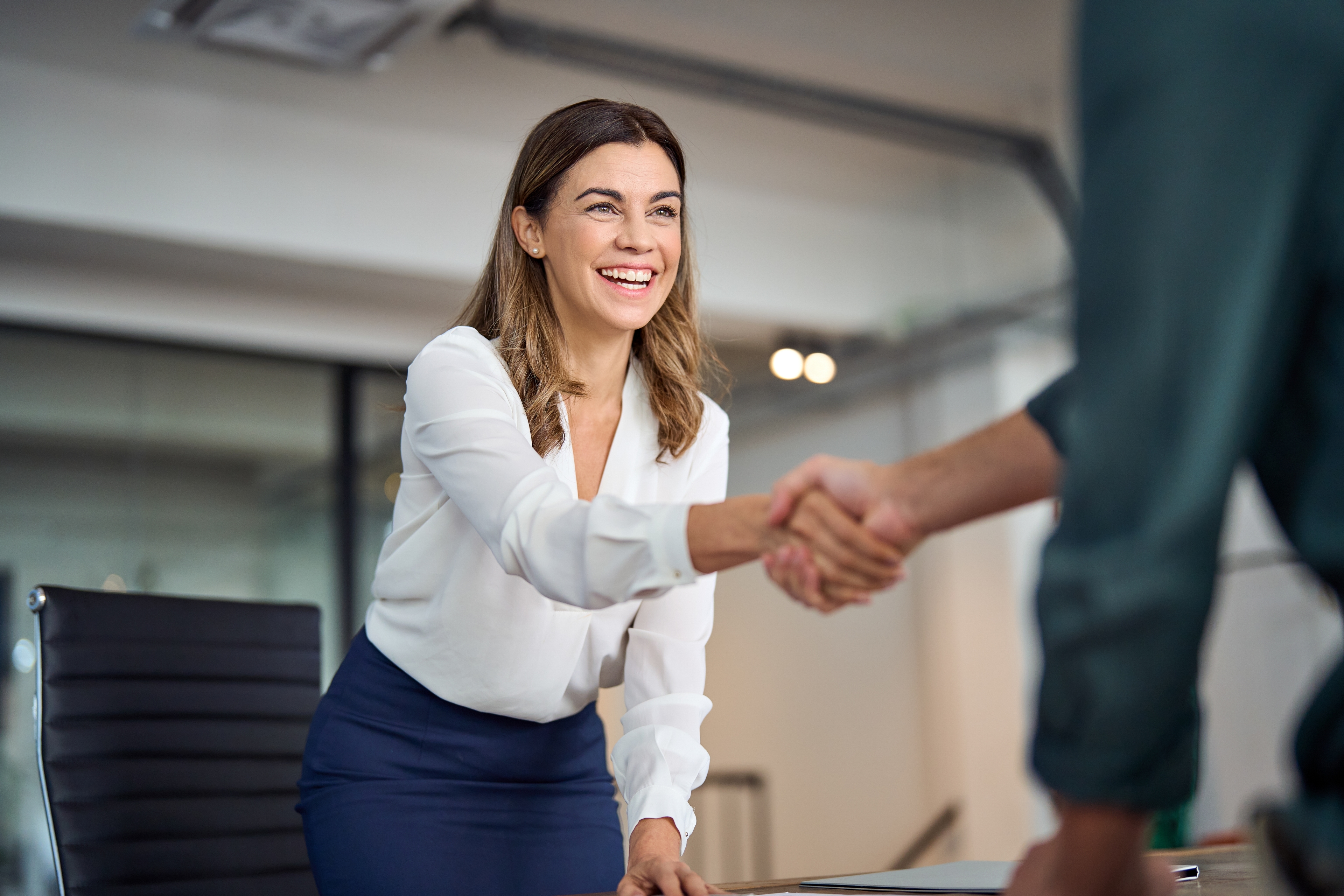 Women leaning over a desk shaking someones hand after just getting a job.