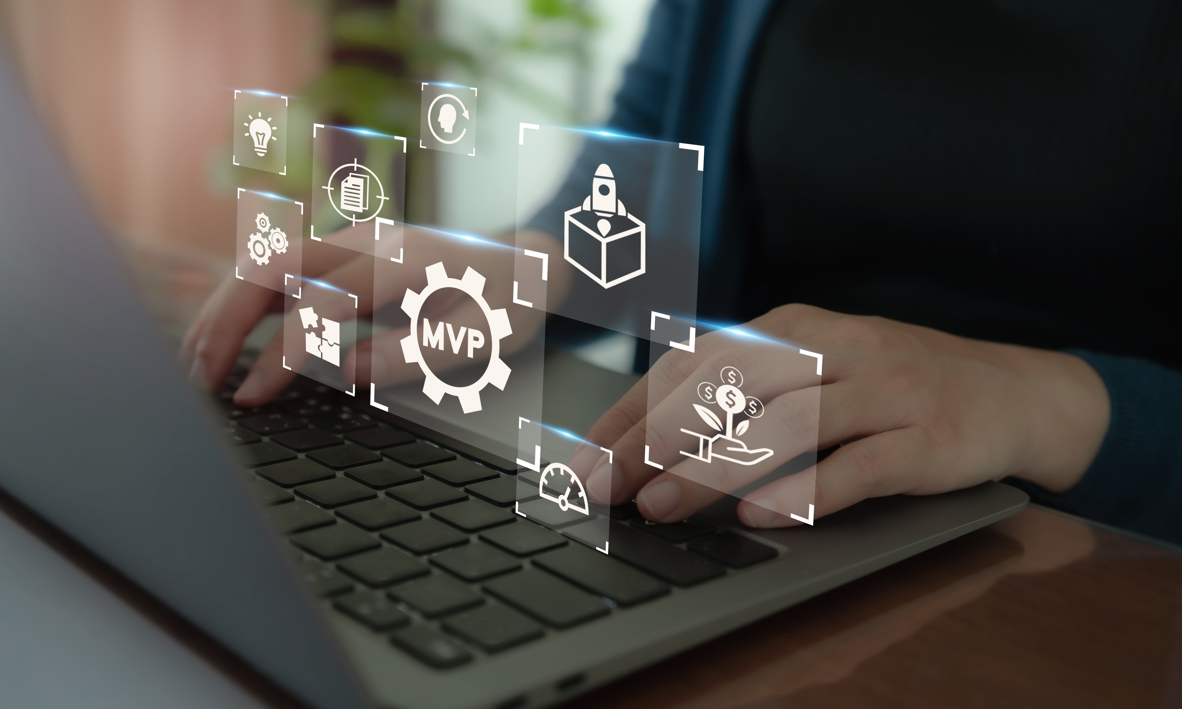 Person typing on a macbook laptop with hovering images of icons indicating they are working on an mvp (minimum viable product)