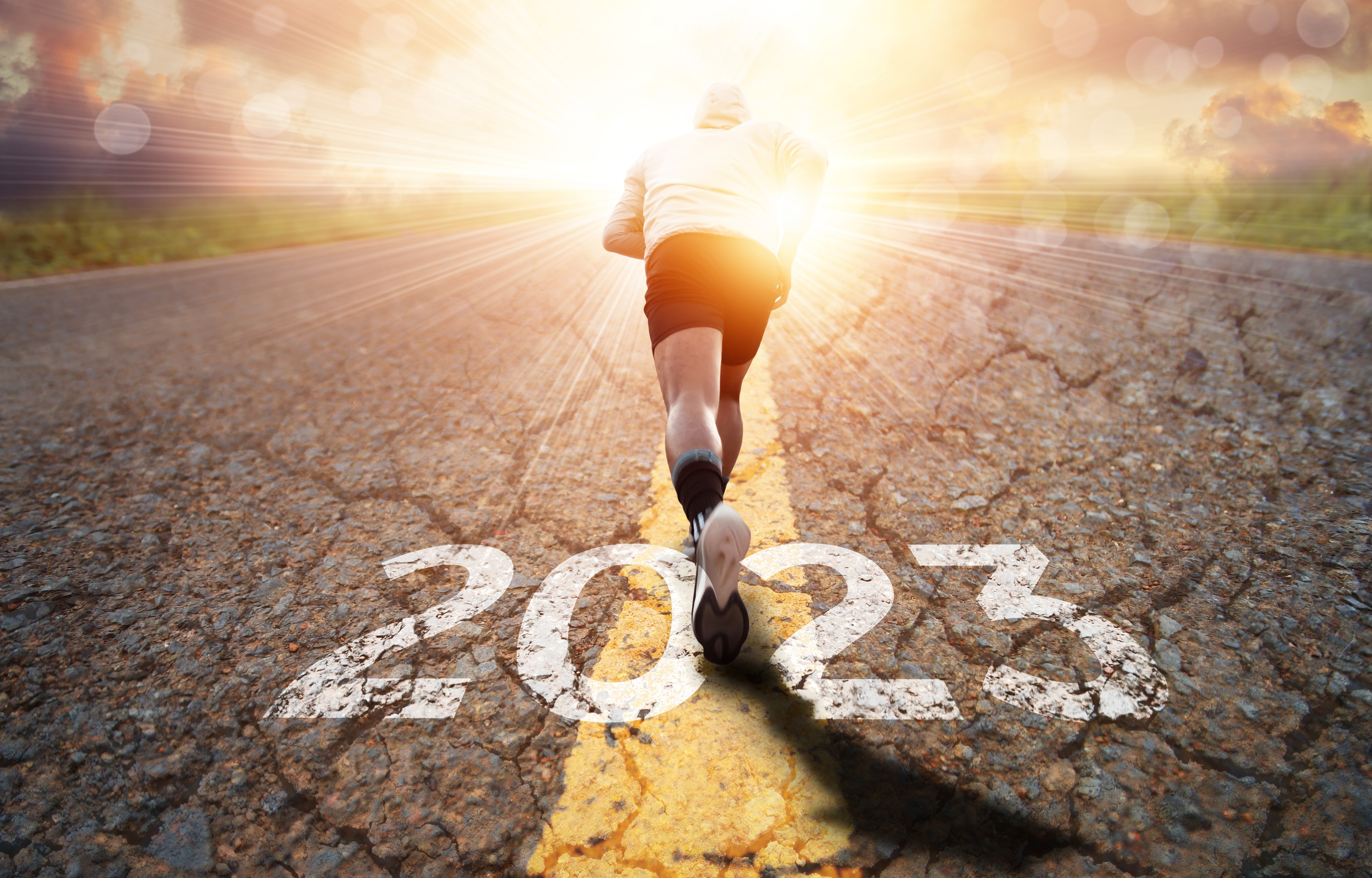 Athlete in the middle of a running motion in the middle of a road. Underneath the althelete is the text of the year 2023.